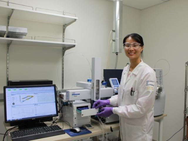 A woman in a lab coat stands in front of some lab equipment